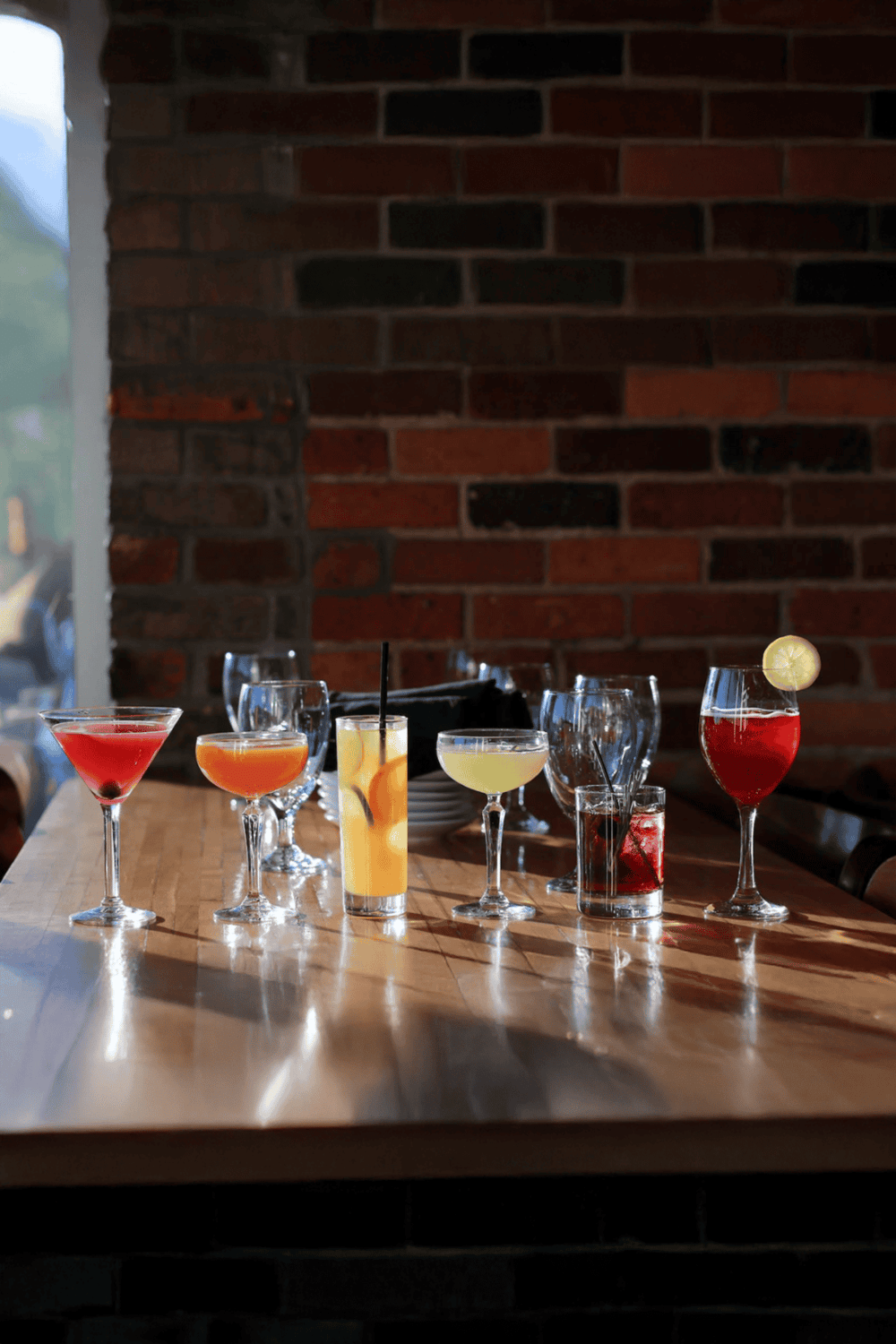 Elegant cocktails on wooden table at restaurant bar with brick wall, stylish drinks, and ambient lighting.