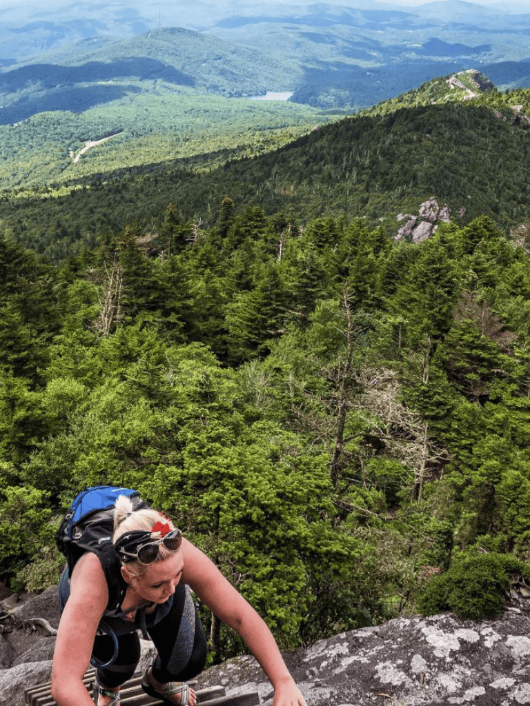 Vast green mountain landscape with a climber ascending rocky terrain amidst lush forest scenery.