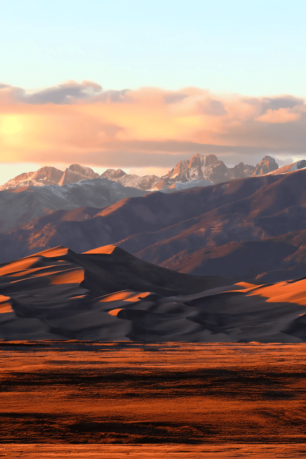 Breathtaking desert landscape with sand dunes and mountain range at sunset, showcasing natural beauty.