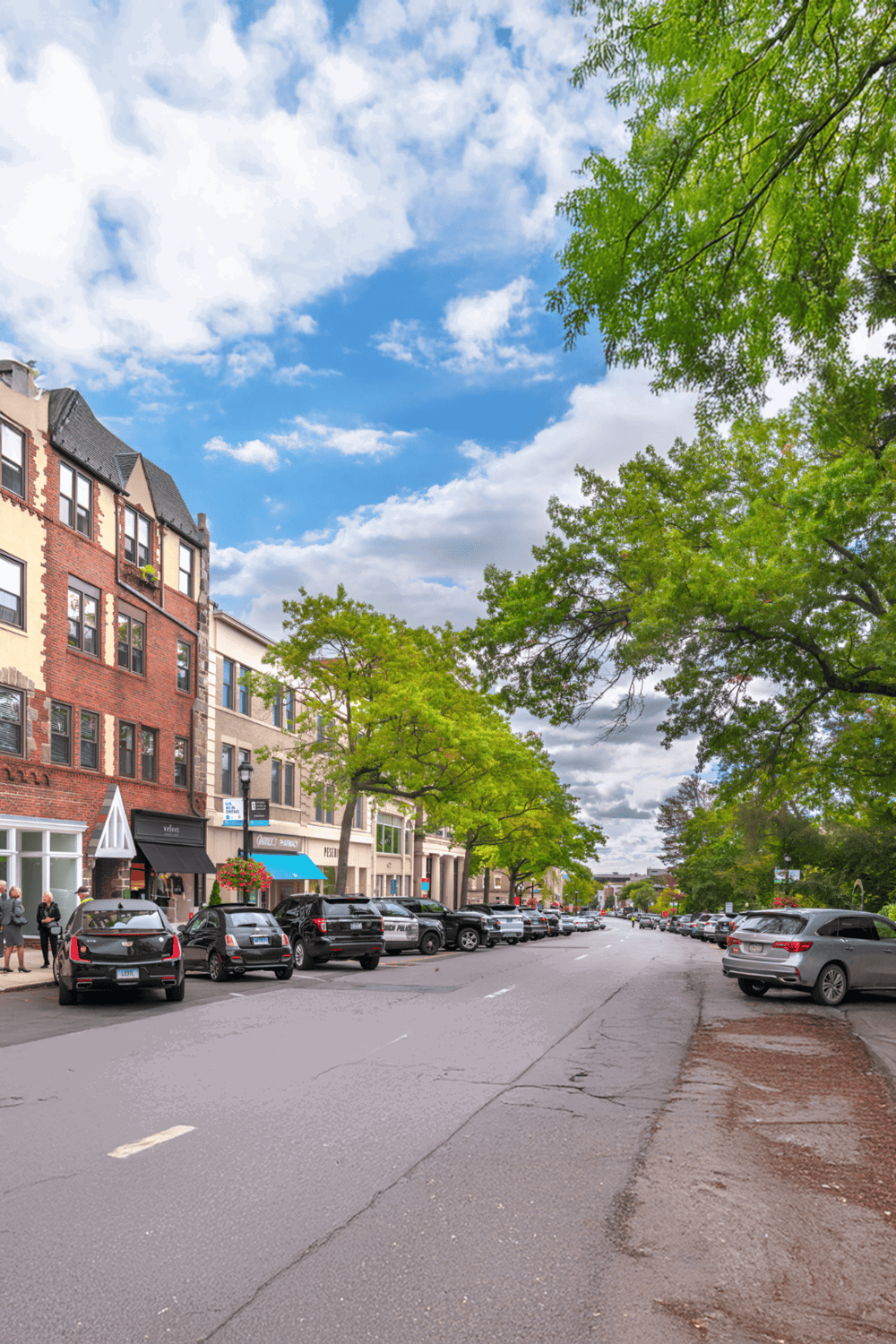Aerial view of downtown street with parking, trees, and historic buildings under blue sky with clouds.