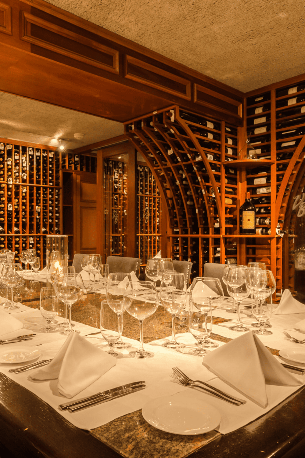 Luxurious wine cellar dinner setup with elegant glassware and wooden wine racks.