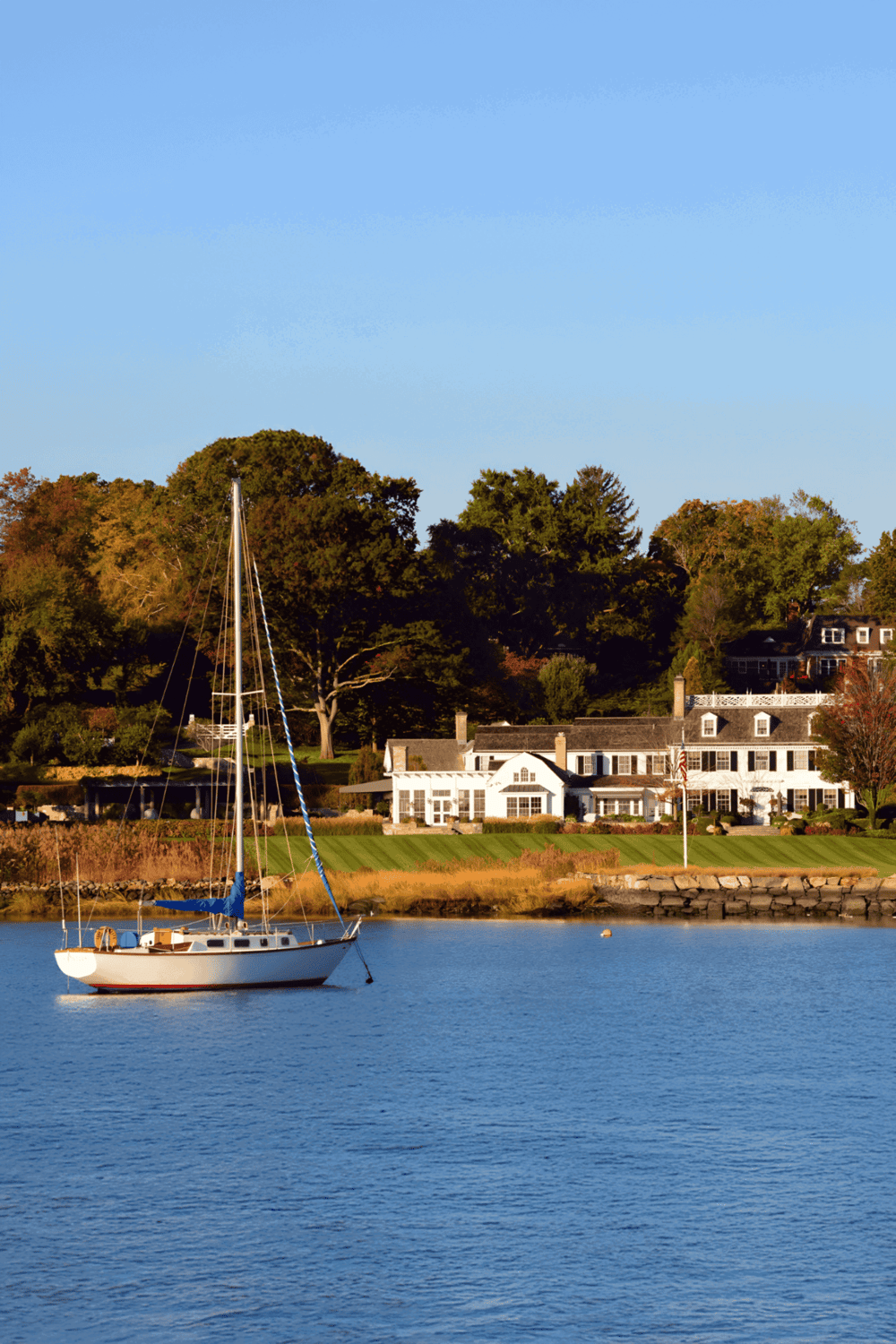 Relaxing waterfront scene with sailboat and upscale homes, perfect for travel and leisure enthusiasts.