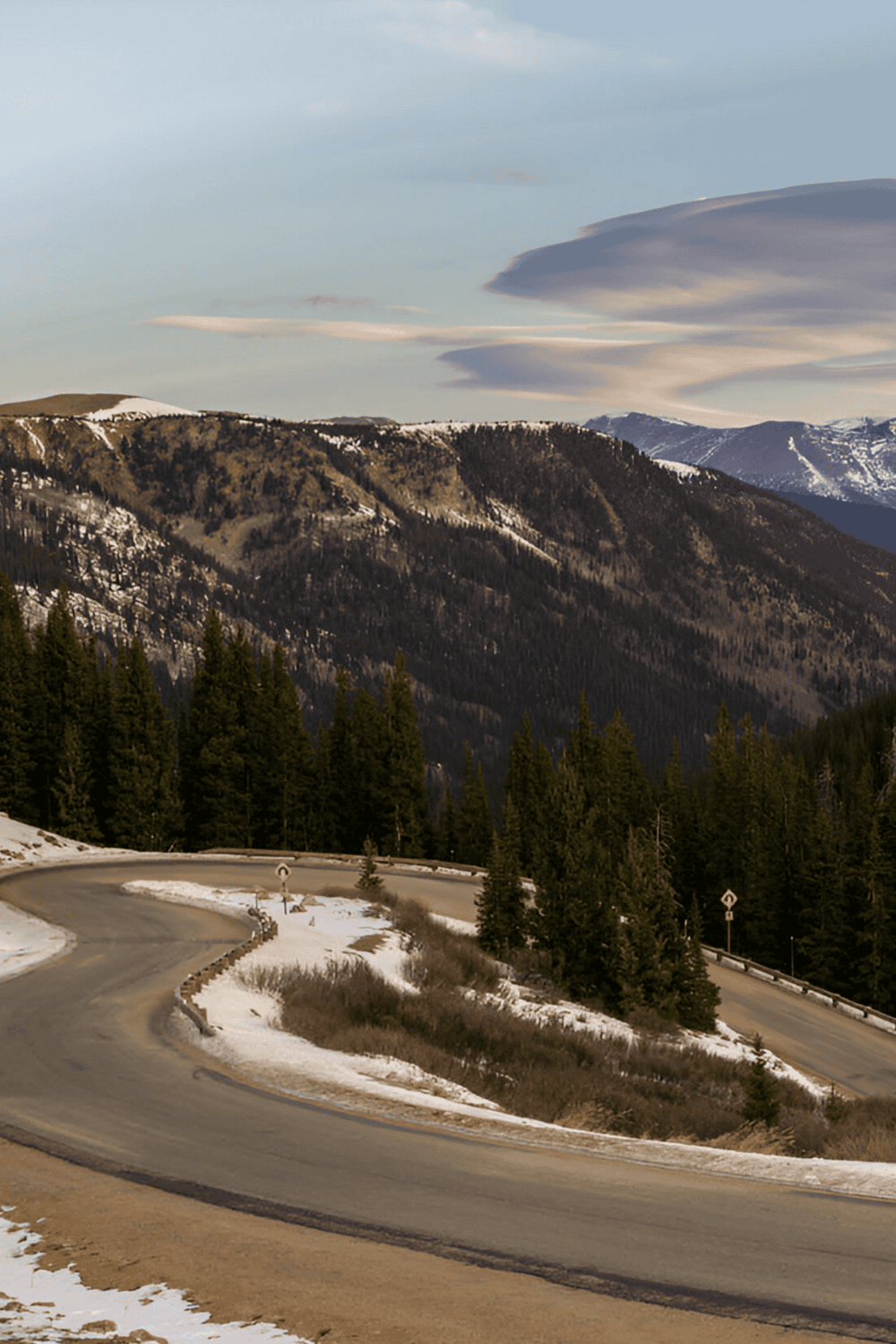 Winding mountain road with snow and pine trees, scenic landscape for travel and adventure.