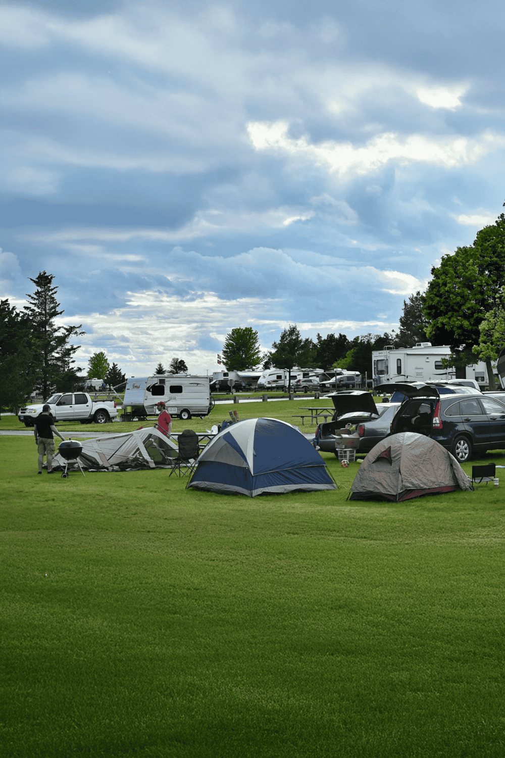 Bright outdoor campground with tents, RVs, and lush green grass under a cloudy sky, perfect for camping trips.