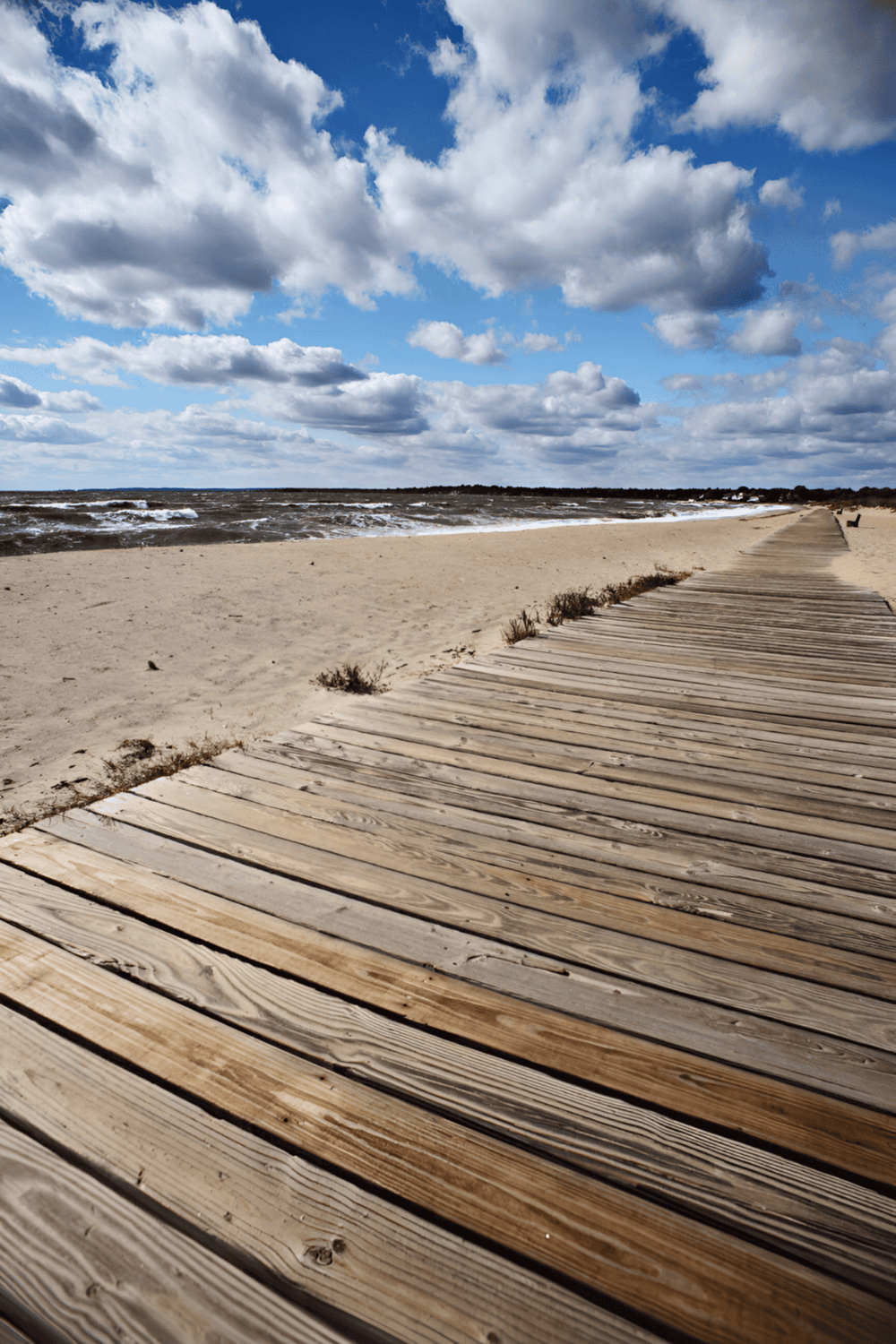 Seaside wooden walkway leading to the ocean on a cloud-filled day, perfect for beach travel and coastal exploration.