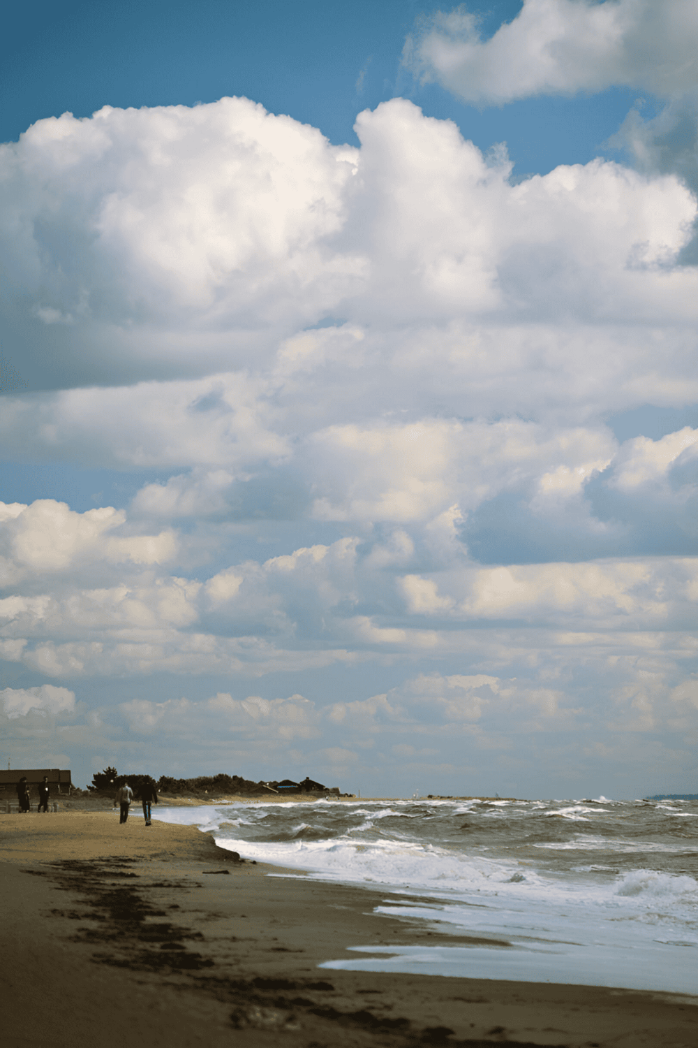 Cloudy sky over beach shoreline with people walking along the coast.