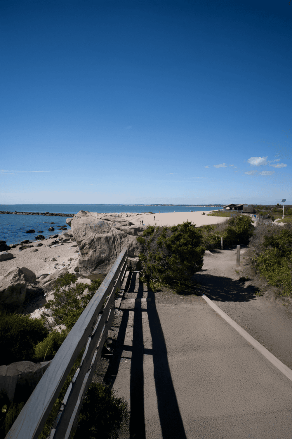 Lakeside coastal pathway with ocean views, rocks, and sunny sky for scenic outdoor exploration.
