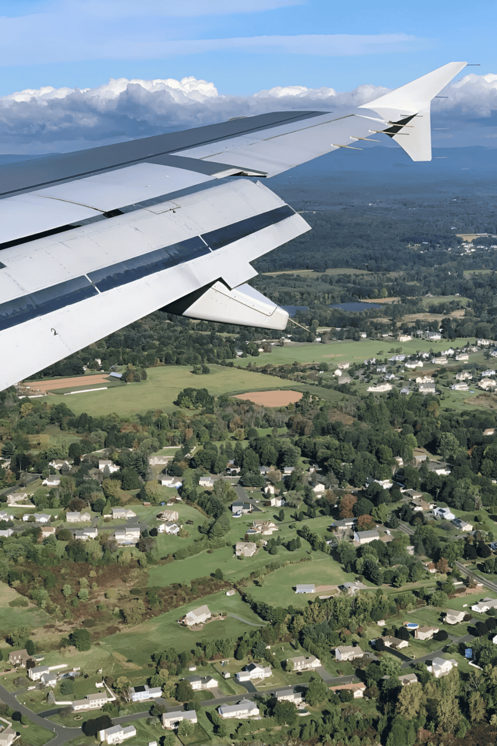 View from airplane window over green suburban landscape and cloudy sky, travel and flight imagery.