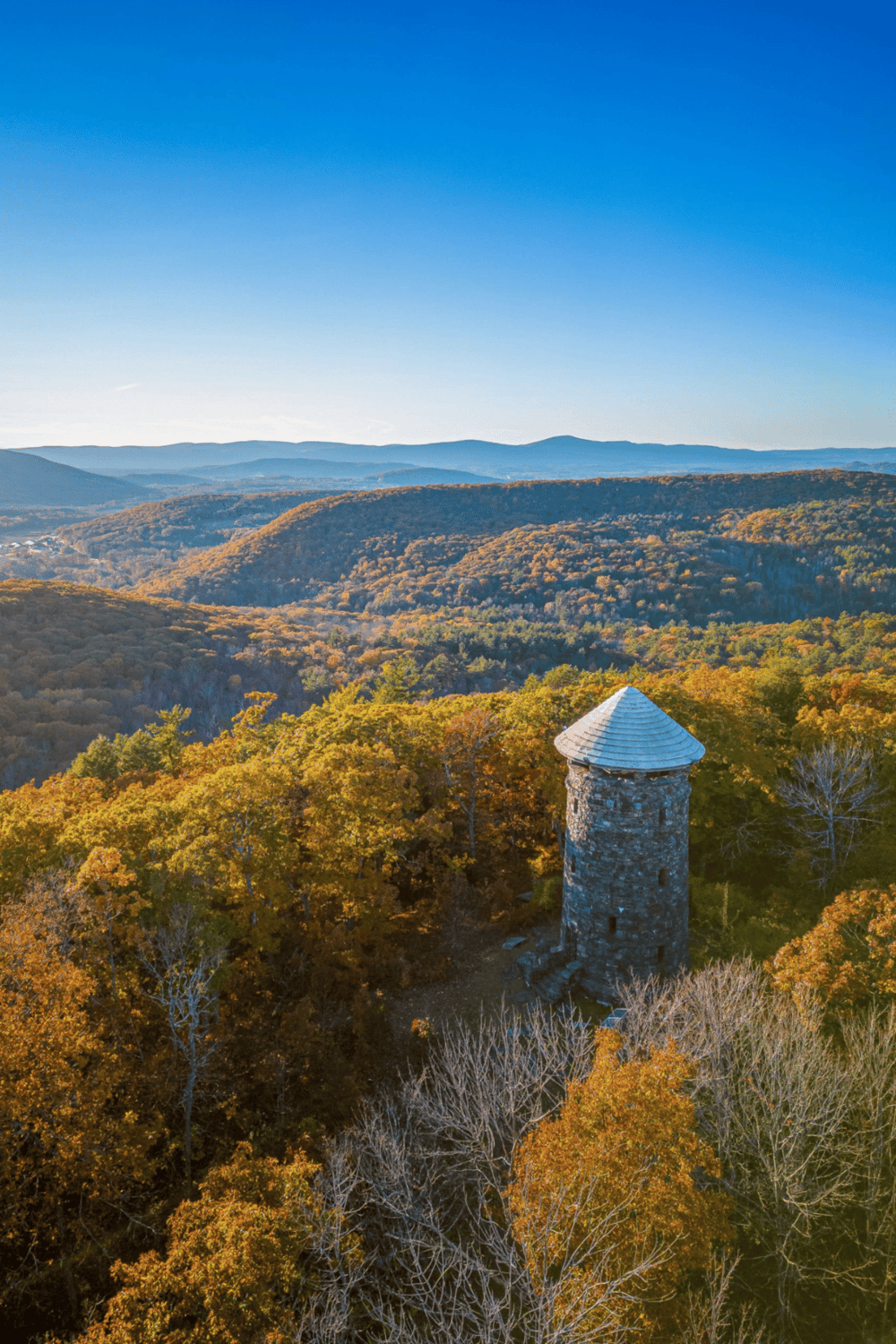 Tall stone tower in colorful autumn forest with mountain backdrop, scenic view for travel and outdoor adventure.