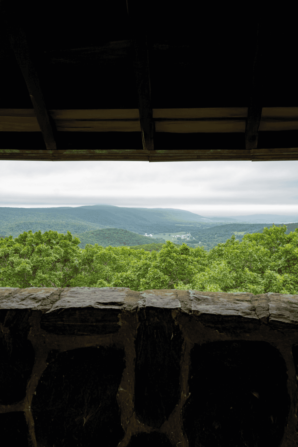 Serene mountain view from a rustic overlook with lush green trees and cloudy sky, perfect for outdoor adventures.