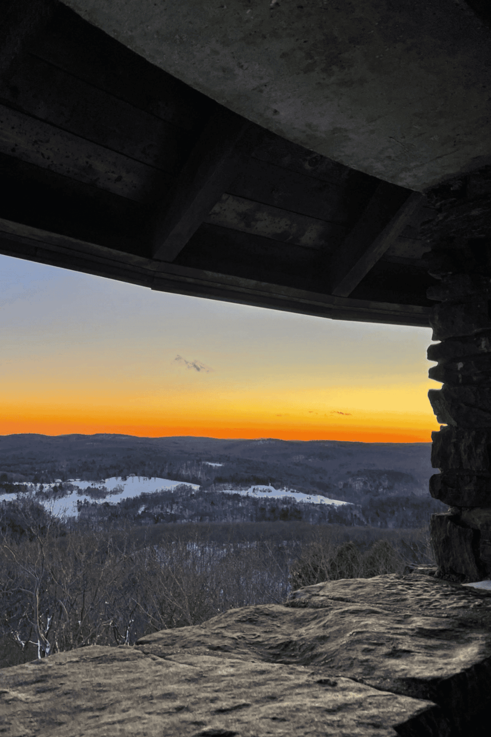 Vast mountain landscape view during sunset in snow-covered terrain from a rustic lookout shelter.