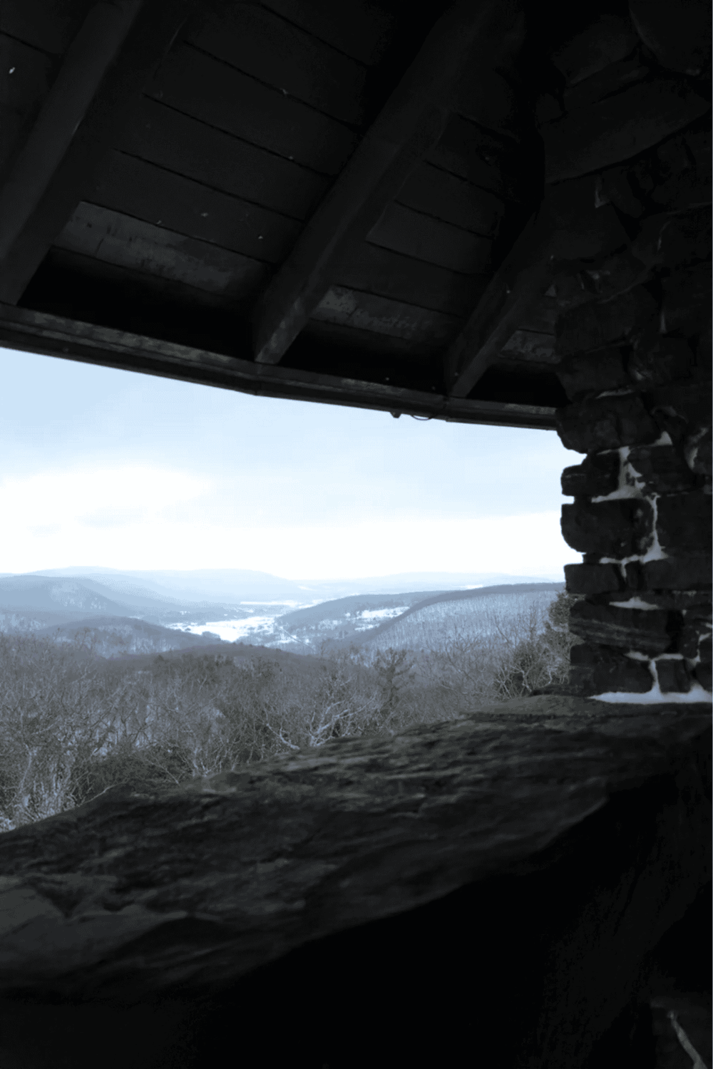 Vantage view of mountainous landscape through rustic wooden shelter in winter.