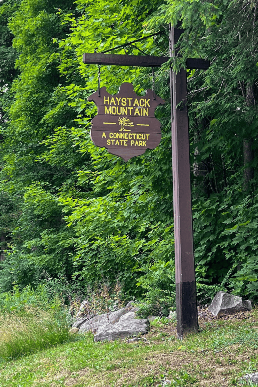 Rustic wooden sign for Haystack Mountain, Connecticut state park, with lush green forest background.