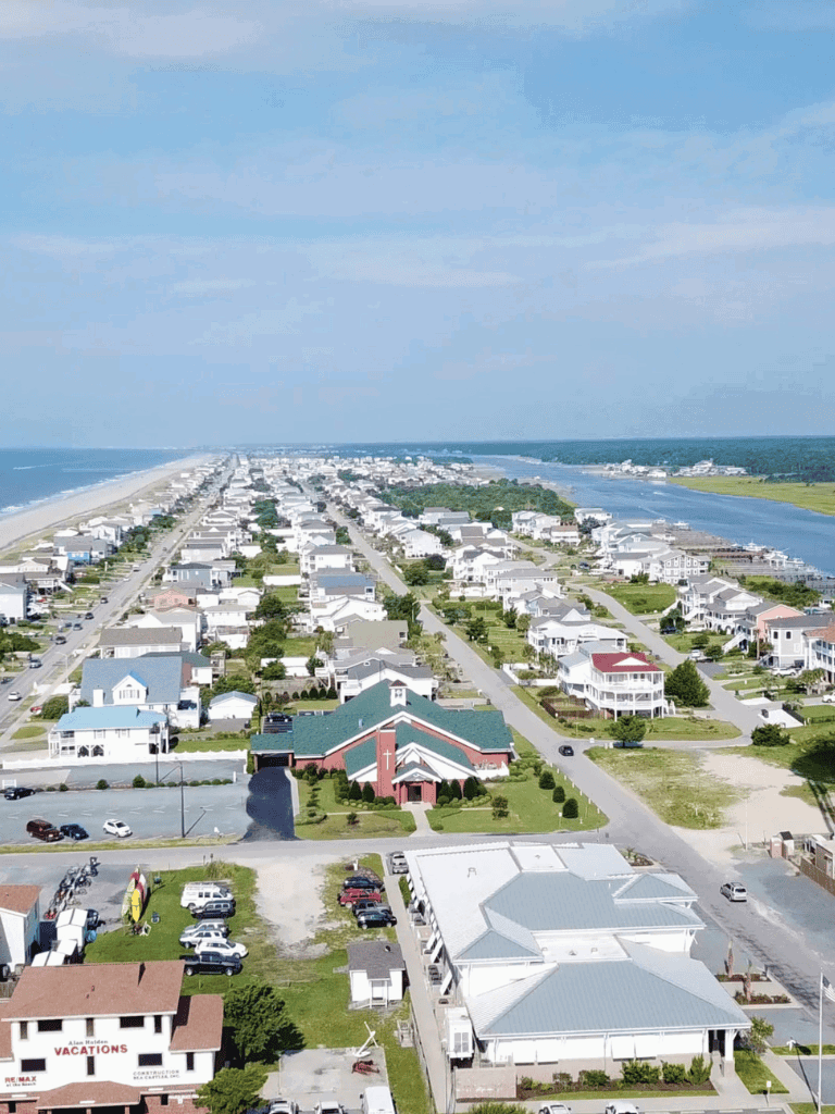 Coastal beachfront neighborhood with houses, church, and parking lot in a scenic seaside location.