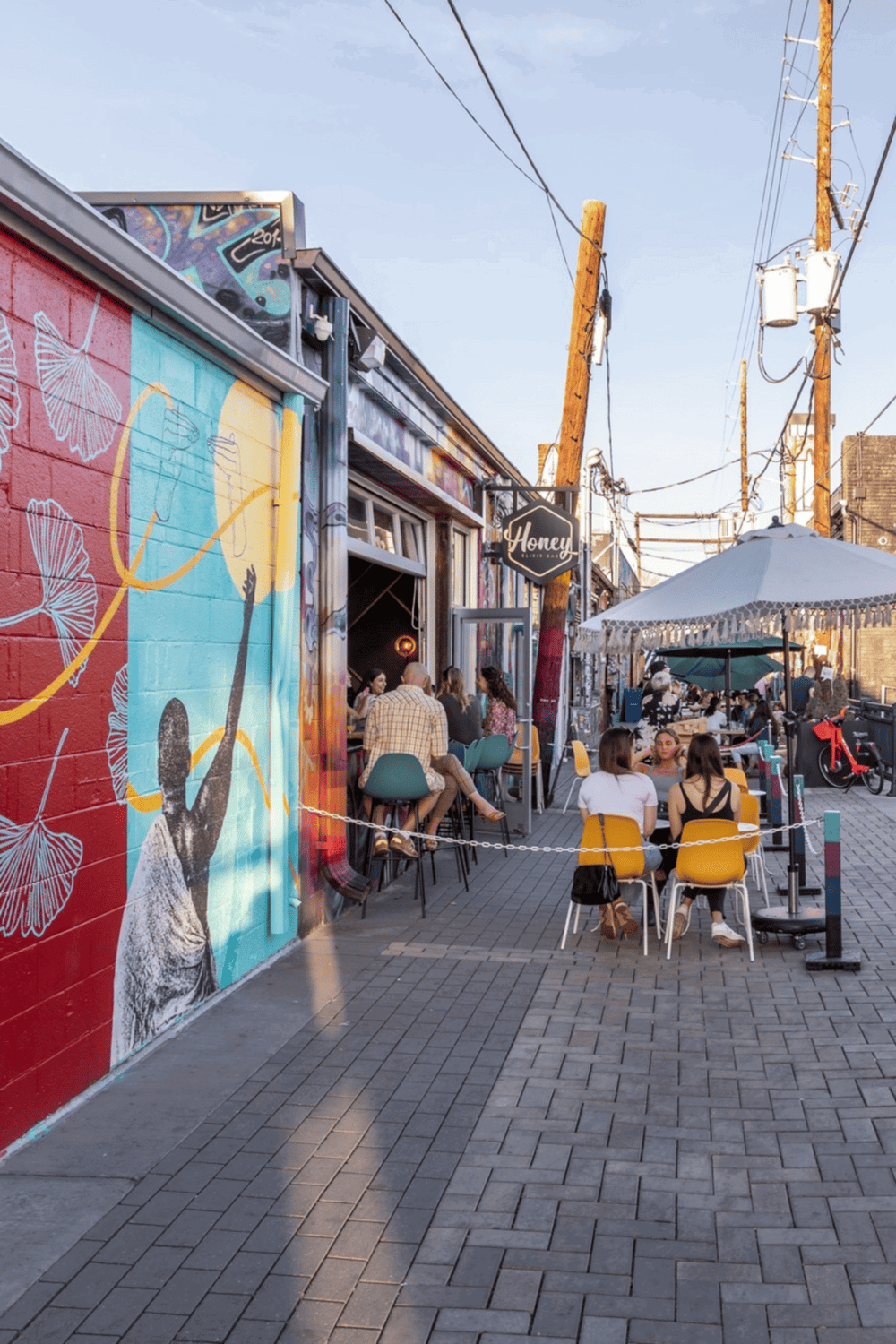 Colorful outdoor dining area with vibrant mural art and social atmosphere in an urban setting.