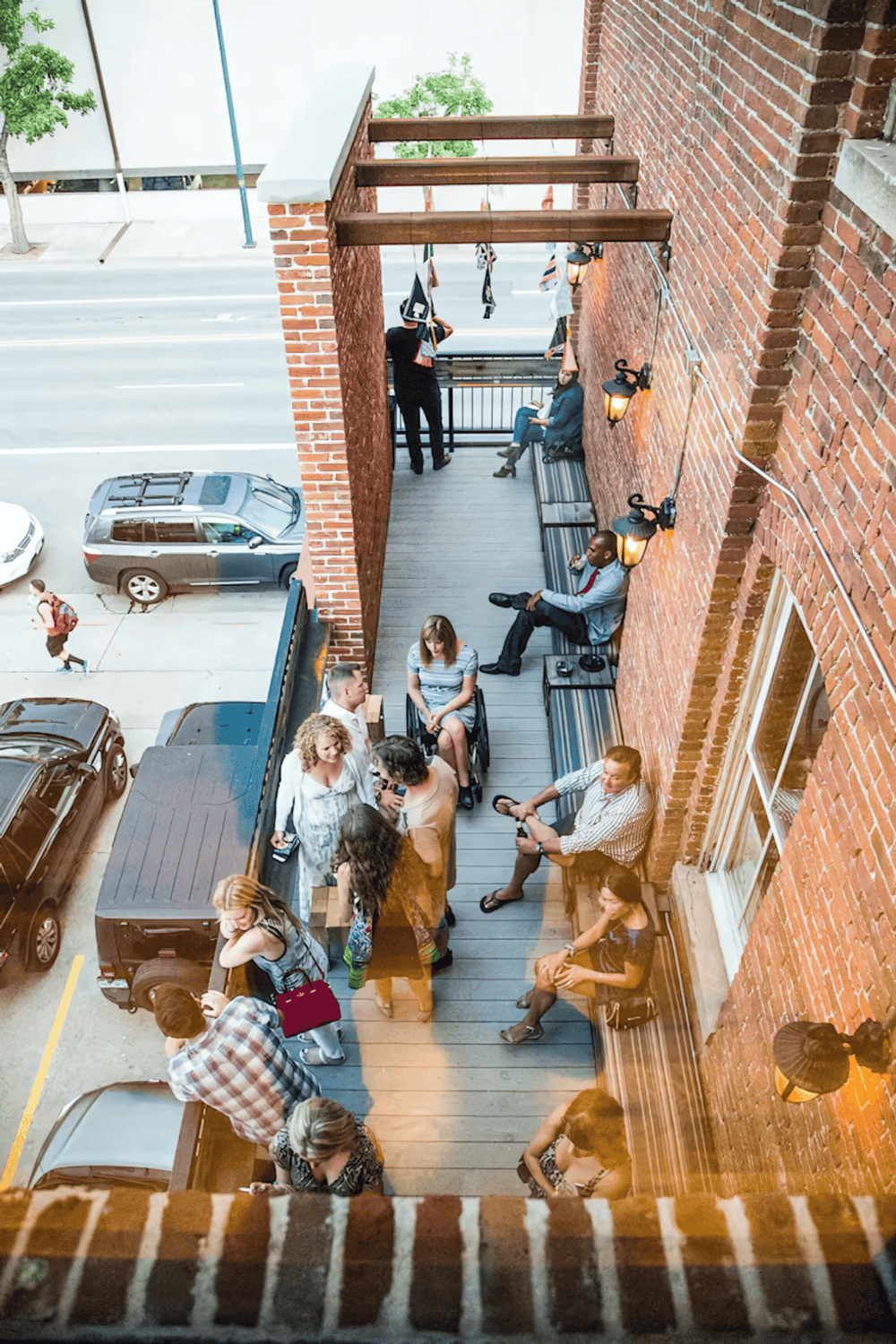 Outdoor city balcony with people networking and relaxing near brick walls and hanging lights.