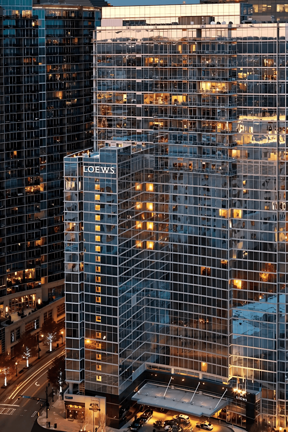 Modern glass skyscraper with illuminated interior offices at dusk, central city location, featuring LOEWS signage.