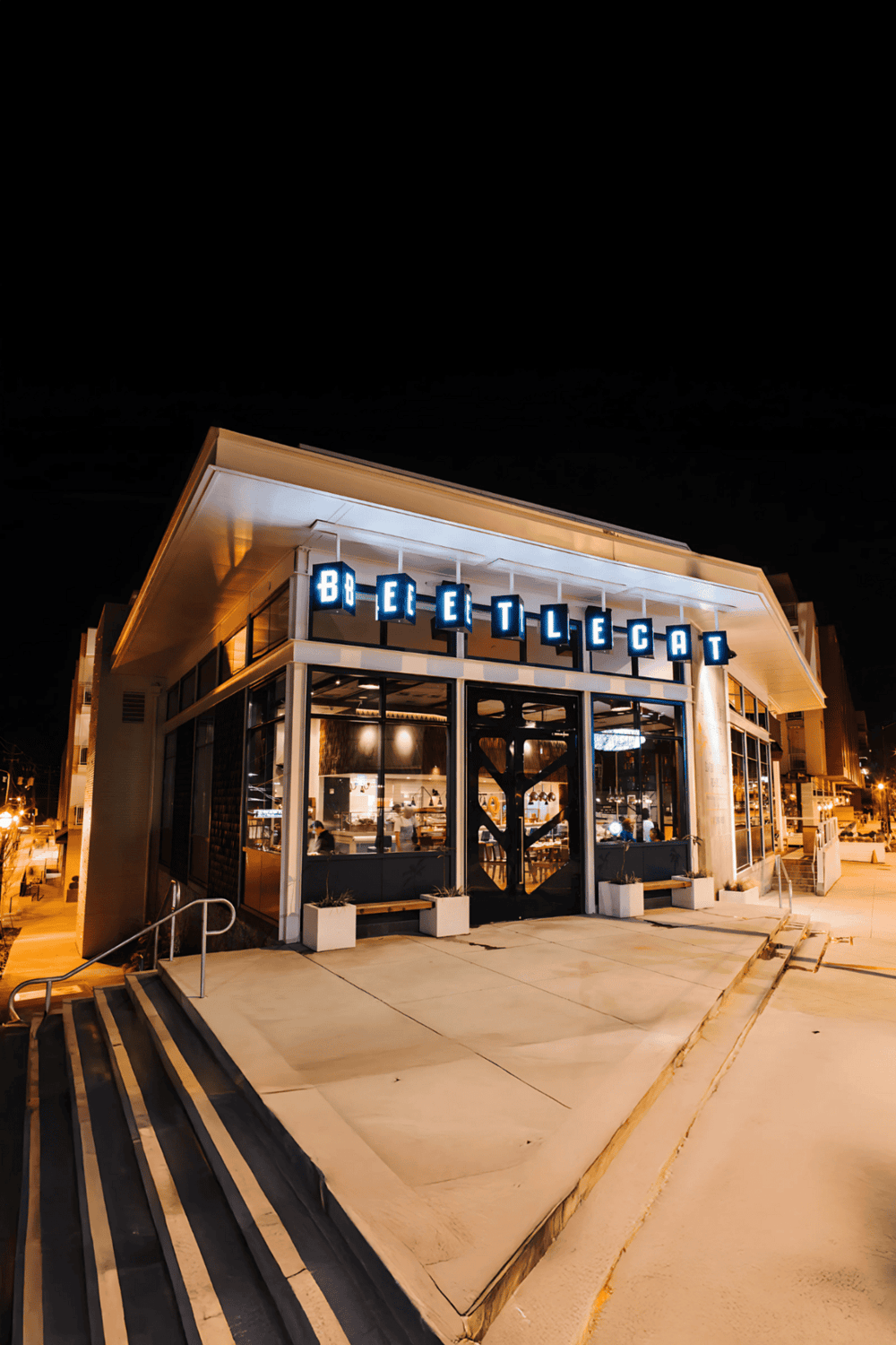 Modern restaurant exterior at night with inviting neon sign, stylish architecture, and outdoor steps.