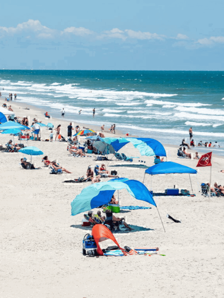 Bright sunny beach with umbrellas, people relaxing, and ocean waves - perfect for vacation planning.