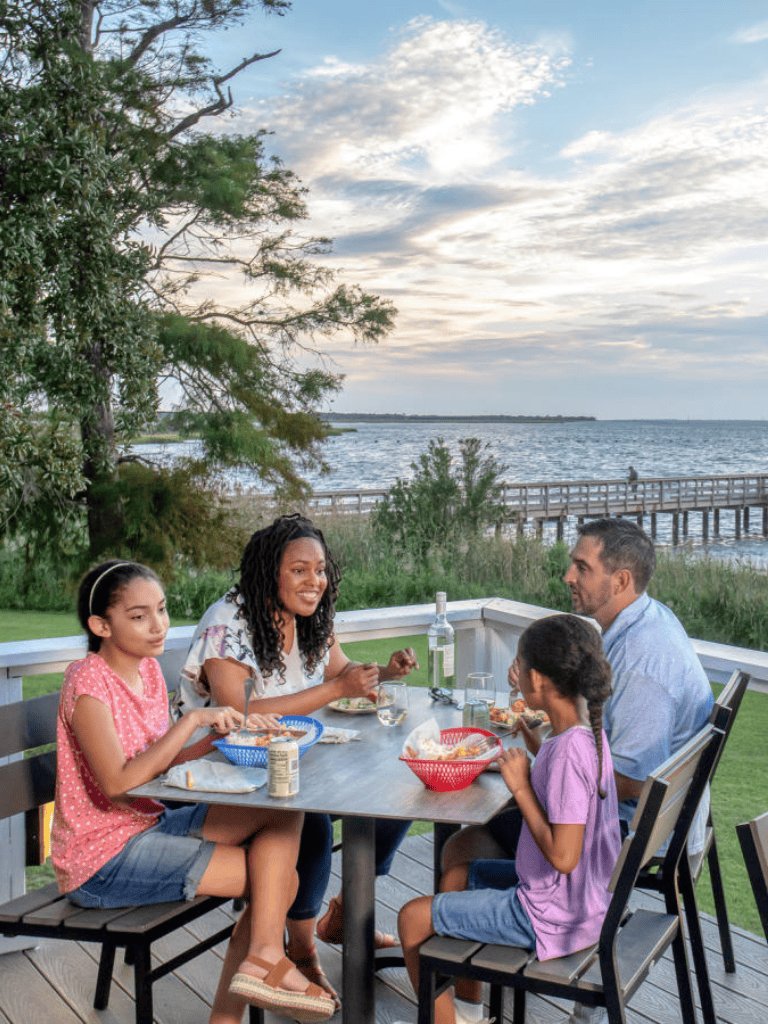Aerial view of a family enjoying dinner outdoor by the water at sunset.