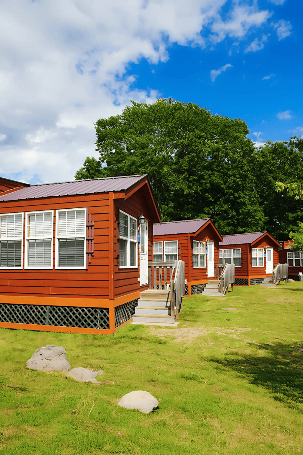 Cozy red cabins with white windows in a lush green outdoor setting under blue sky with clouds.
