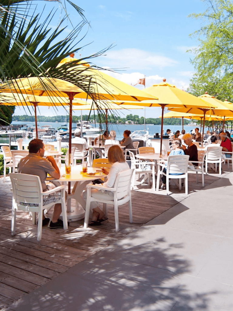 Relaxing lakeside dining with yellow umbrellas and boats in the background, perfect for food, drinks, and scenic views.