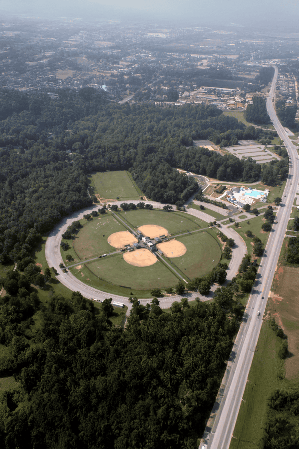 Aerial view of park with baseball fields, pool, and surrounding greenery, showcasing outdoor recreation and community spaces.