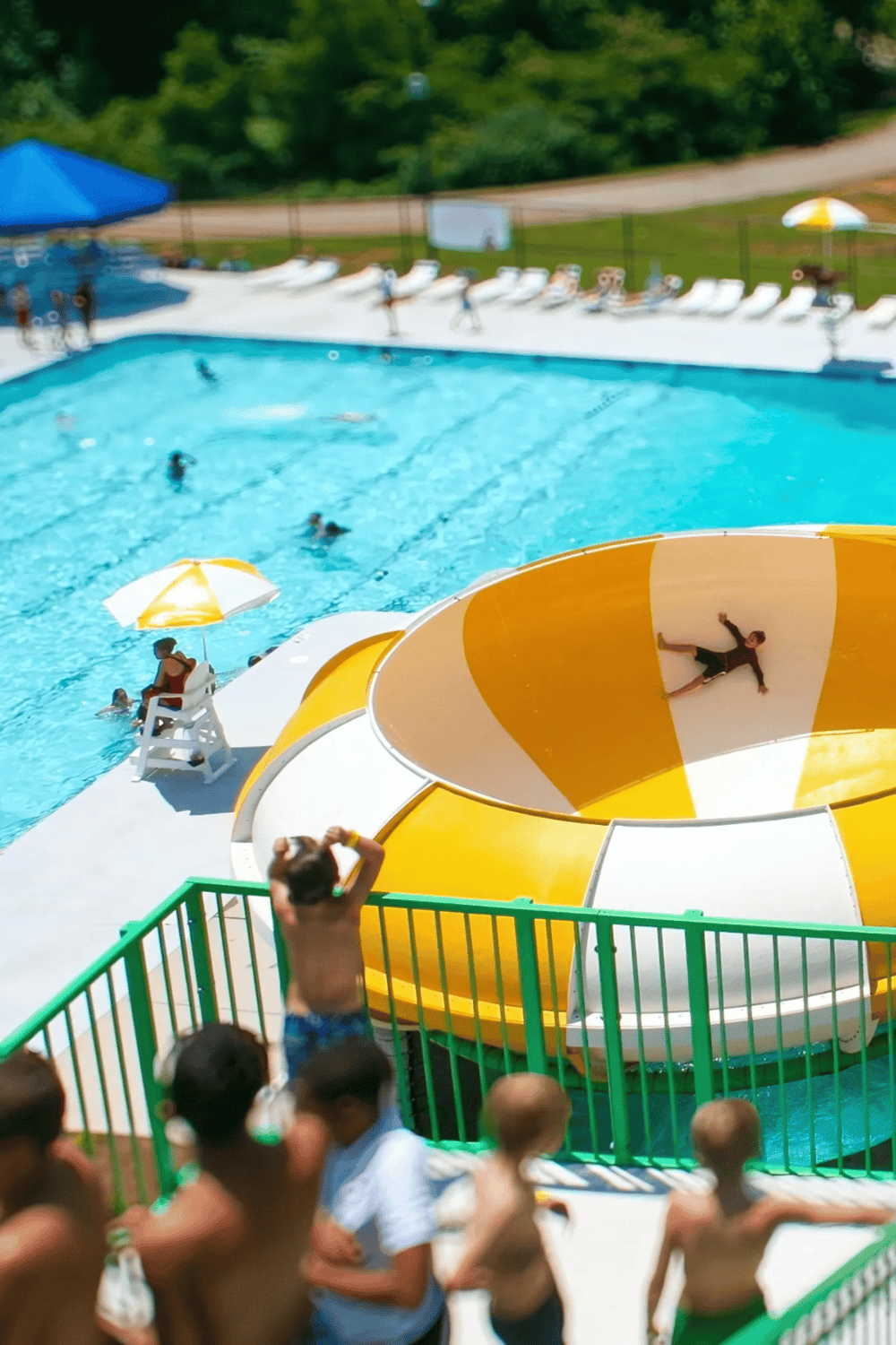 Kids enjoying a water slide and swimming pool at a summer resort with lush greenery.