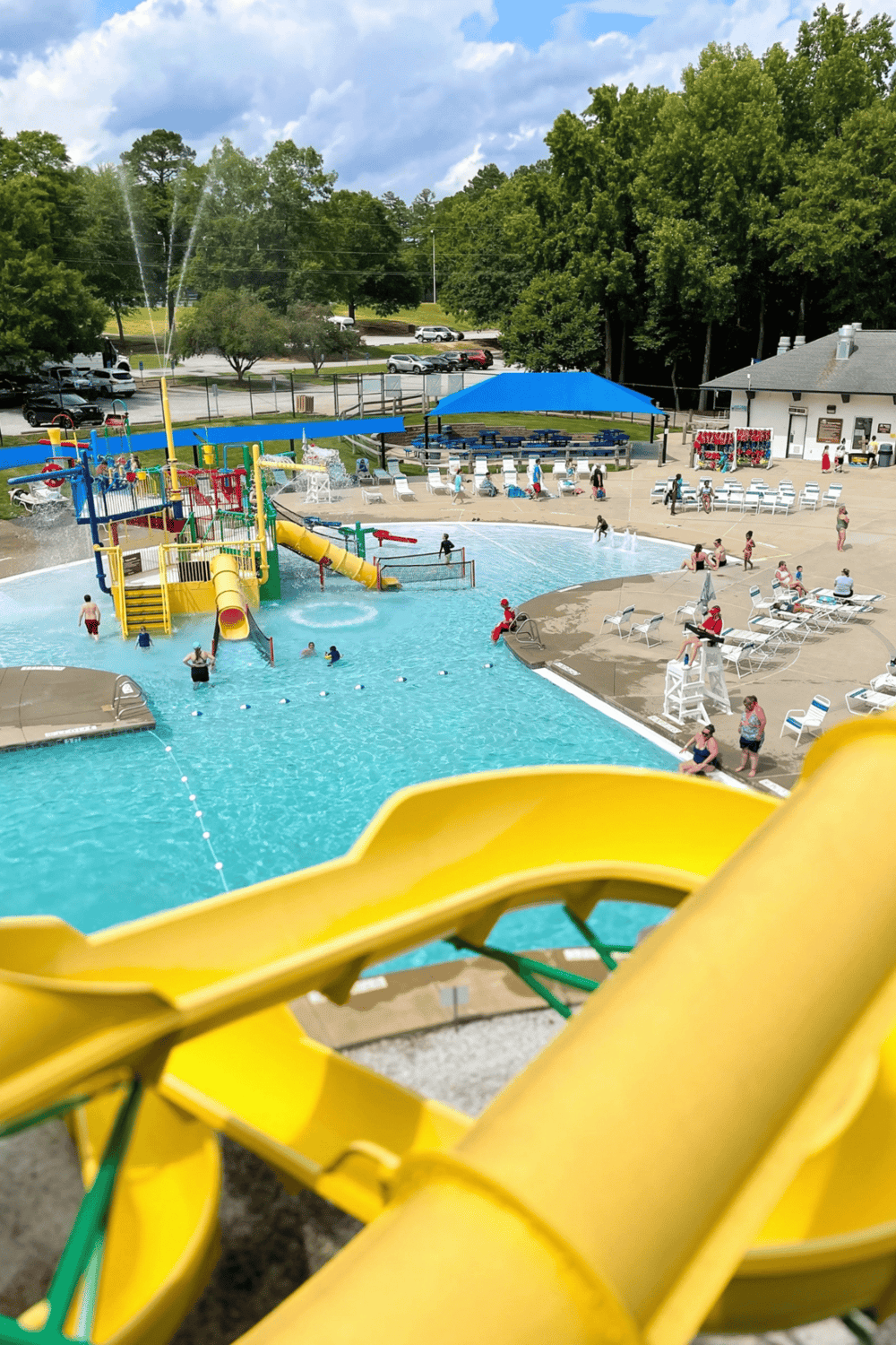 Colorful water park with slides and kids enjoying the pool, surrounded by seating and lush green trees.