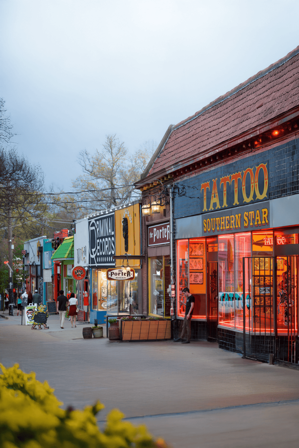 Colorful street view featuring tattoo shops, bars, and local businesses in an urban neighborhood.
