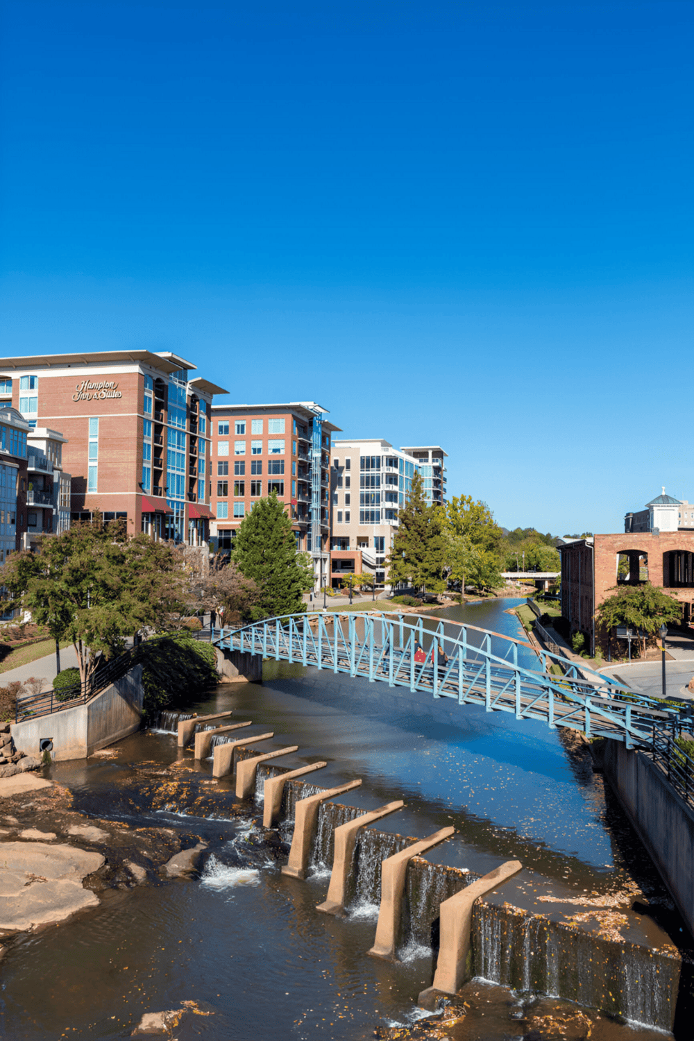 Urban riverfront with modern apartment buildings and a decorative bridge in a vibrant cityscape.
