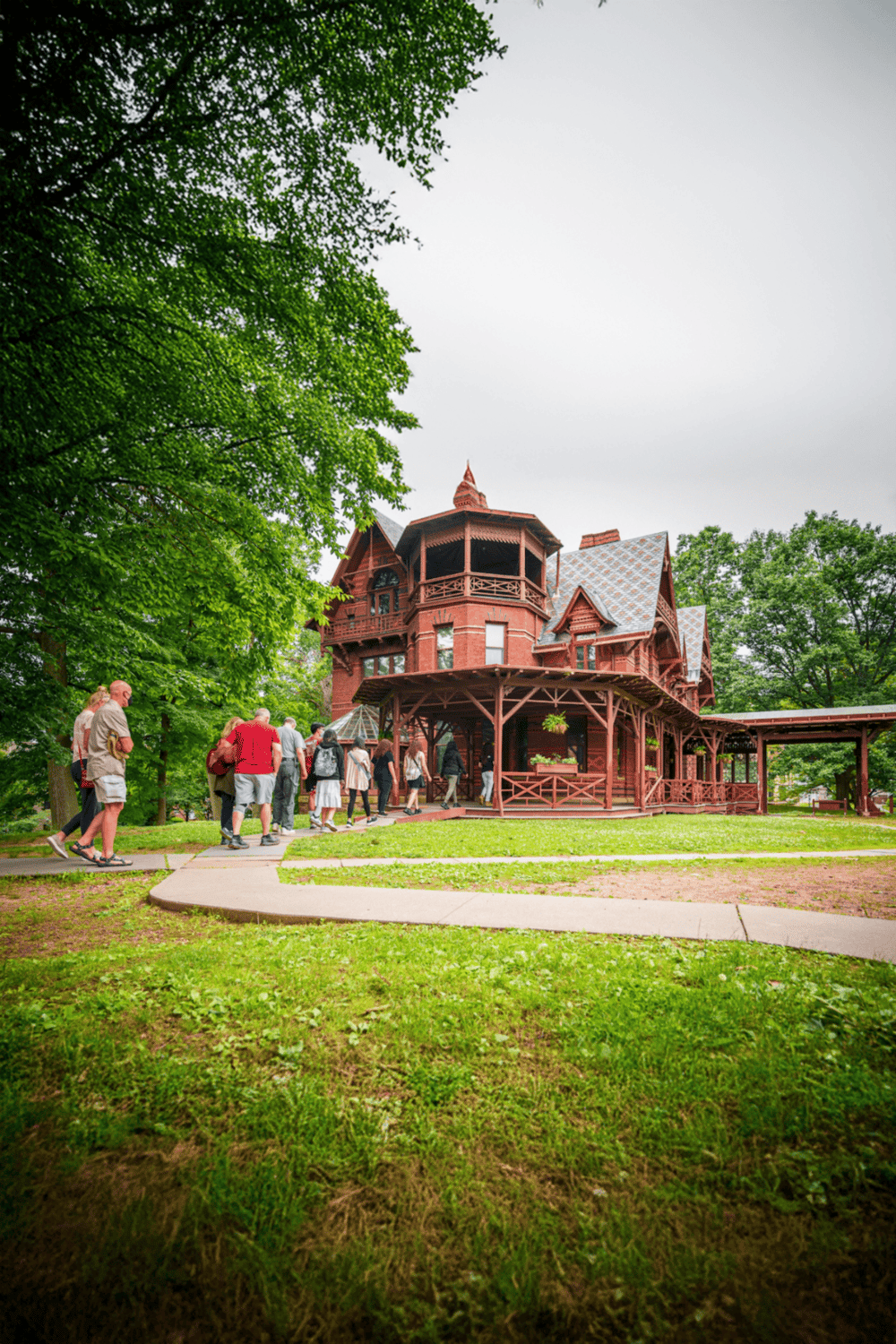 Victorian-style house in a park with visitors, lush greenery, and overcast sky, showcasing community and historic architecture.