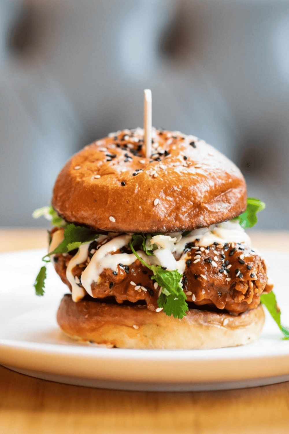 Crispy chicken sandwich with lettuce, mayonnaise, and sesame seeds on a toasted bun.