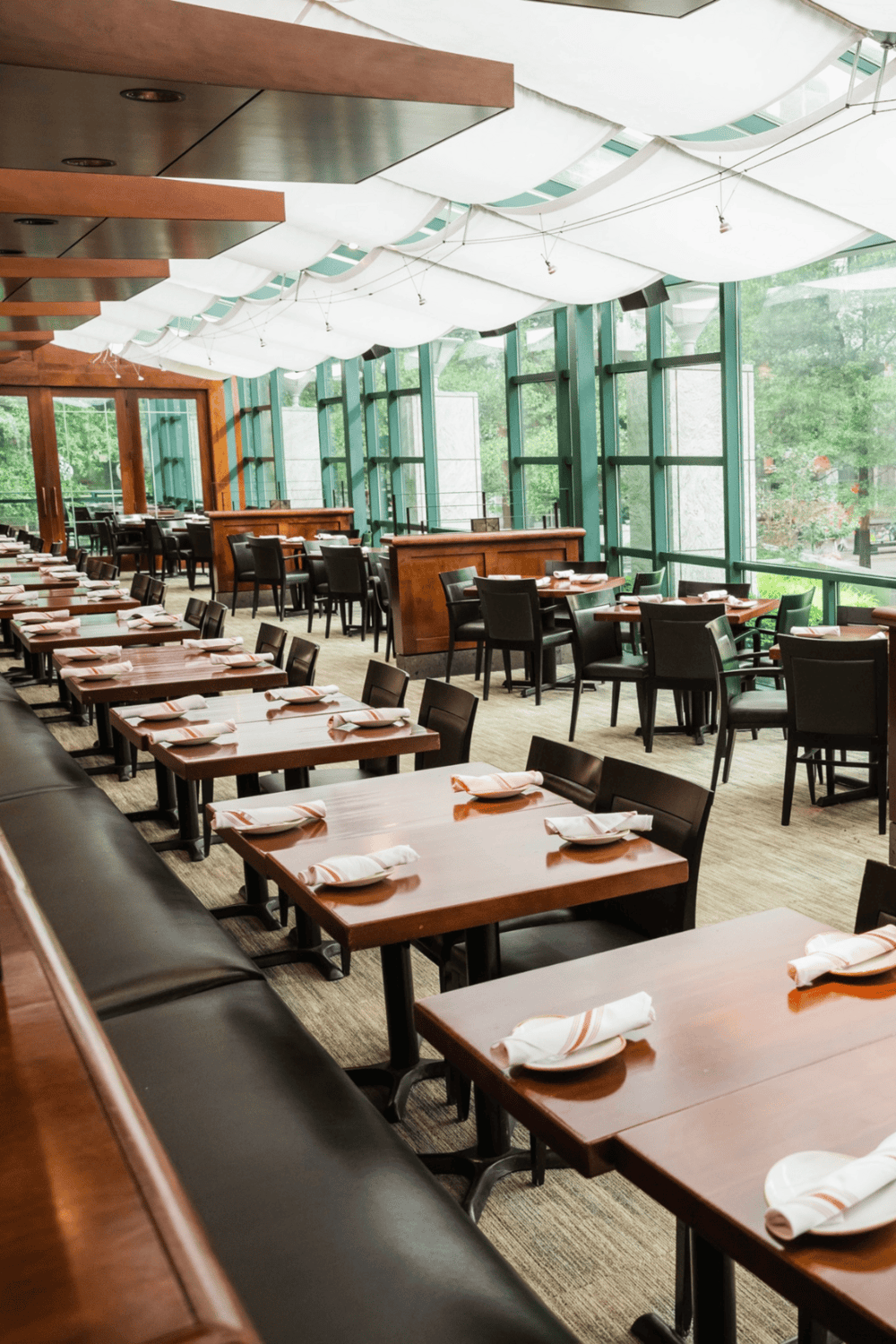 Cozy modern restaurant interior with large windows, wooden accents, and neatly set tables for dining.