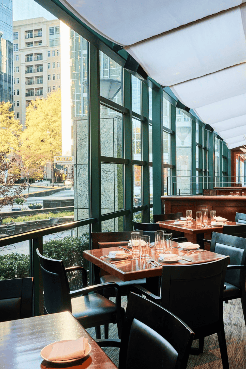 Modern restaurant interior with large glass windows and city views, stylish dining setup.