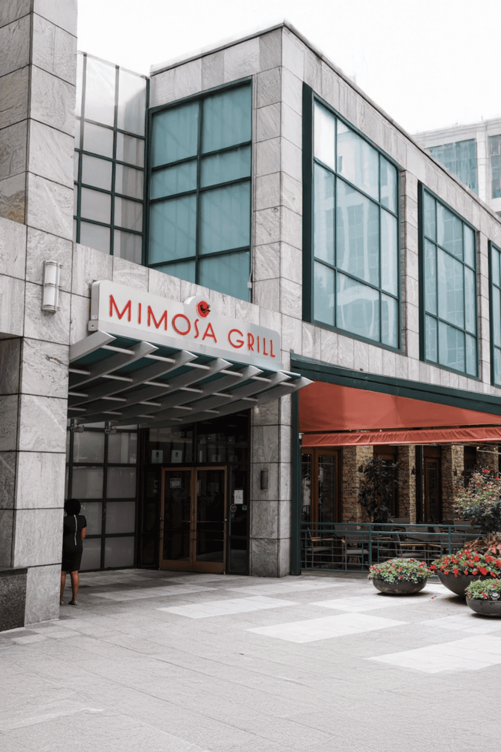 Elegant building exterior with MIMOSA GRILL restaurant signage, modern urban architecture, and outdoor patio.