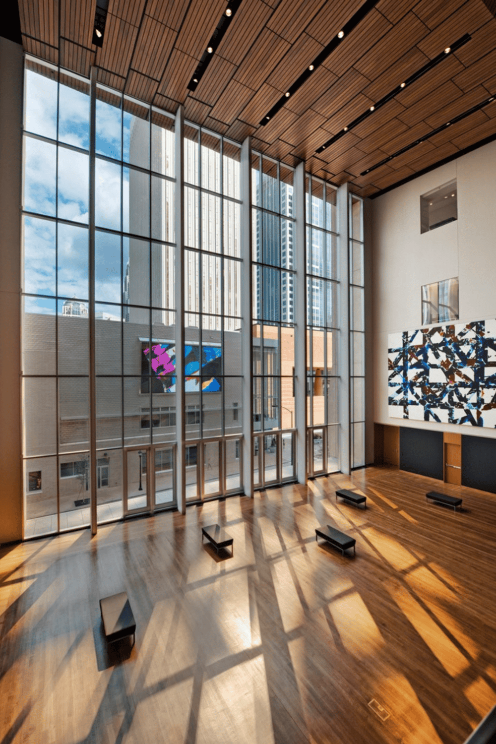 Bright modern lobby with large glass windows and city skyline views, featuring sleek wooden accents and contemporary artwork.