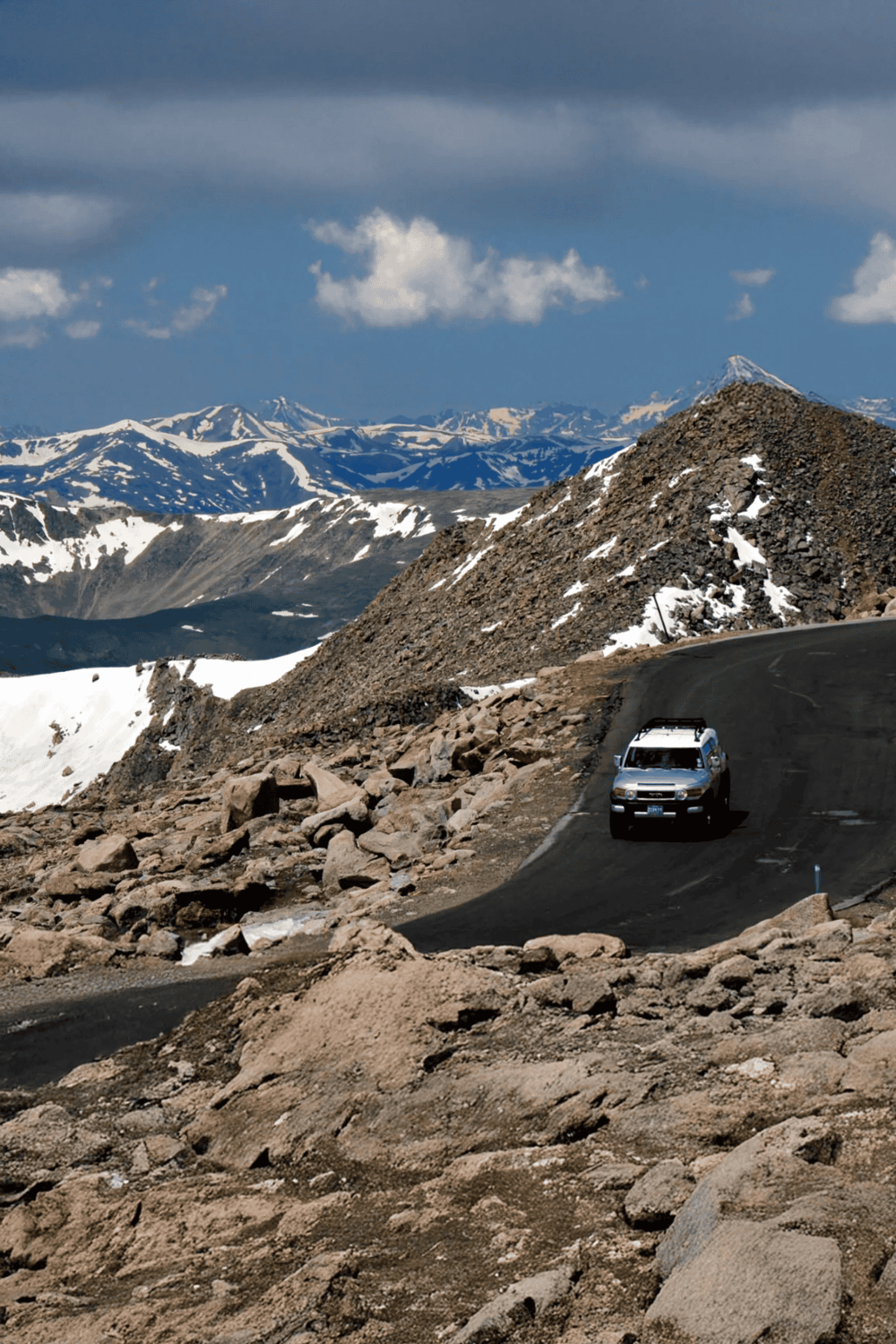 Scenic mountain road with rugged terrain and snow-capped peaks in the background.