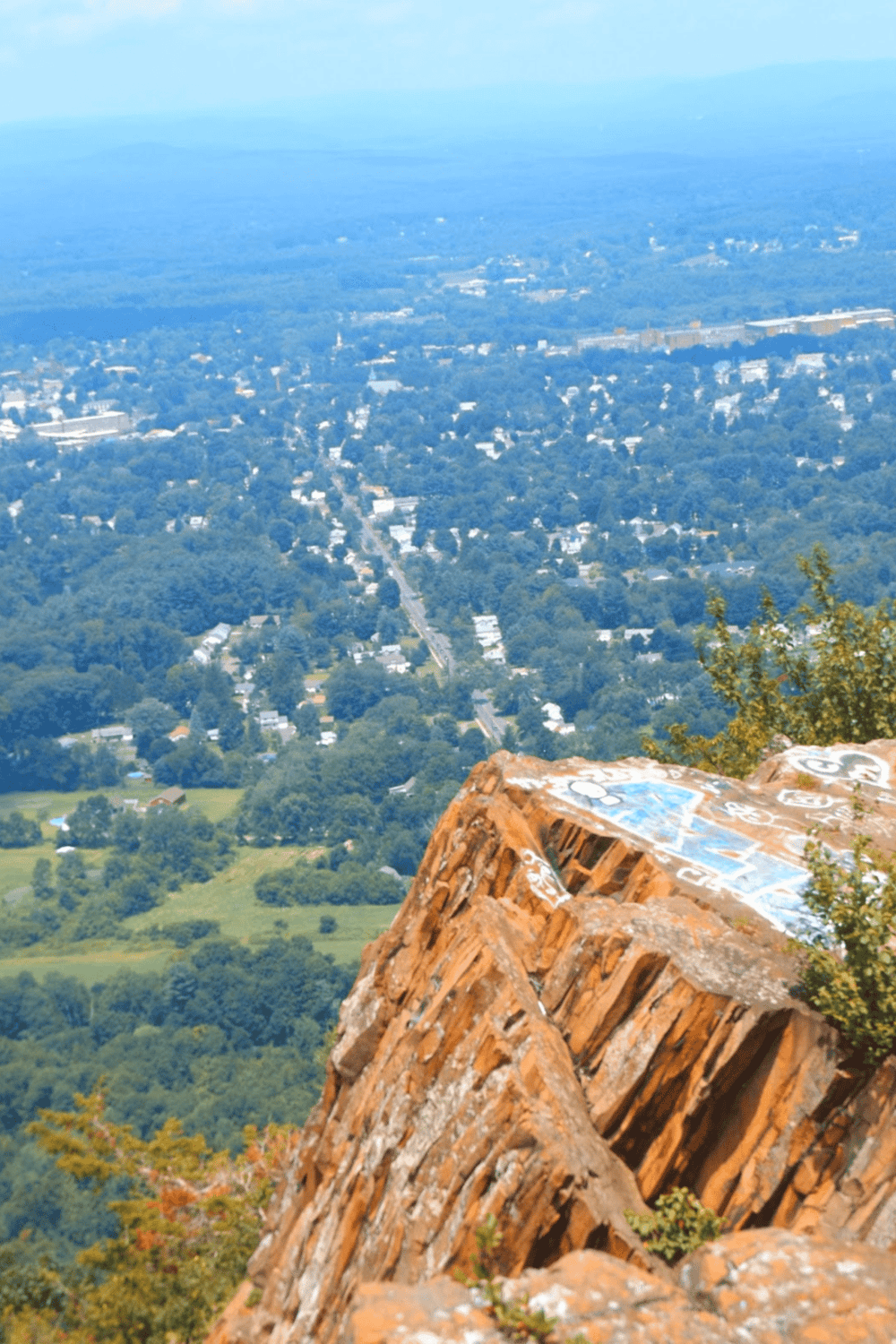 Panoramic view of a city from a mountain summit with graffiti-covered rock in the foreground.