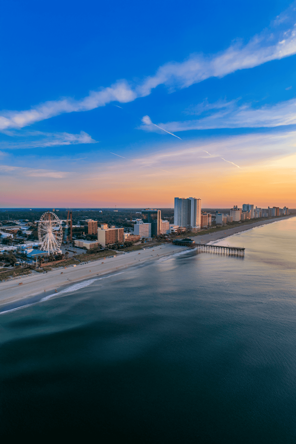Vibrant aerial view of Atlantic City skyline, beach, and amusement park at sunset, showcasing cityscape and coastal attractions.