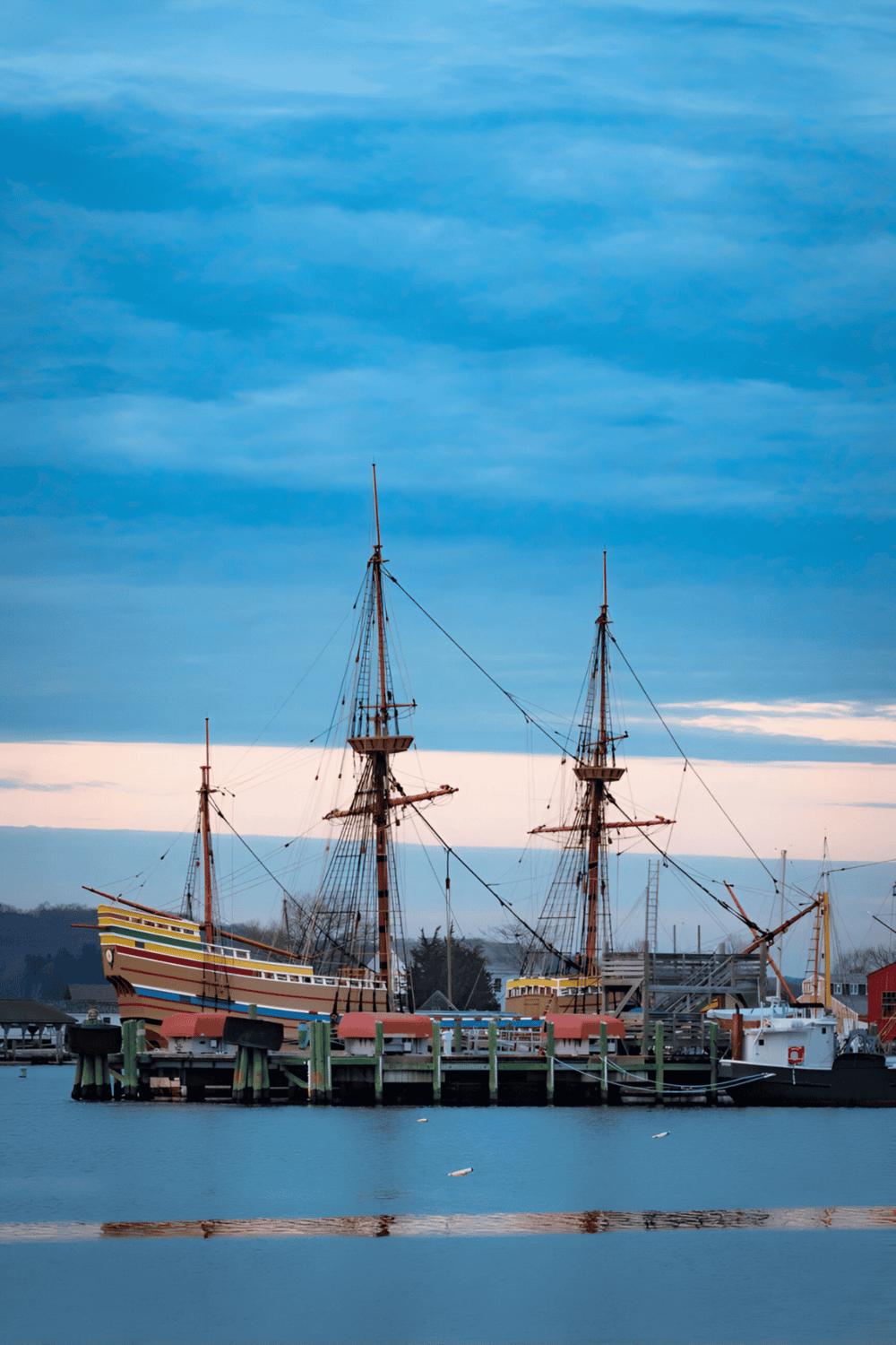 1. Historic sailing ships docked at waterfront marina on calm water at sunset.