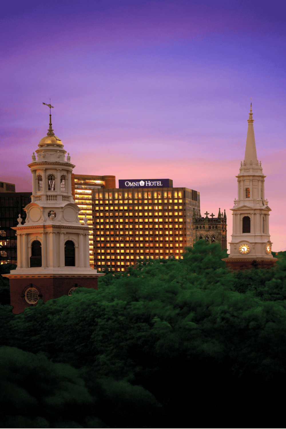Historic downtown skyline with prominent church steeples and Omni Hotel at sunset, showcasing city attractions and travel destinations.