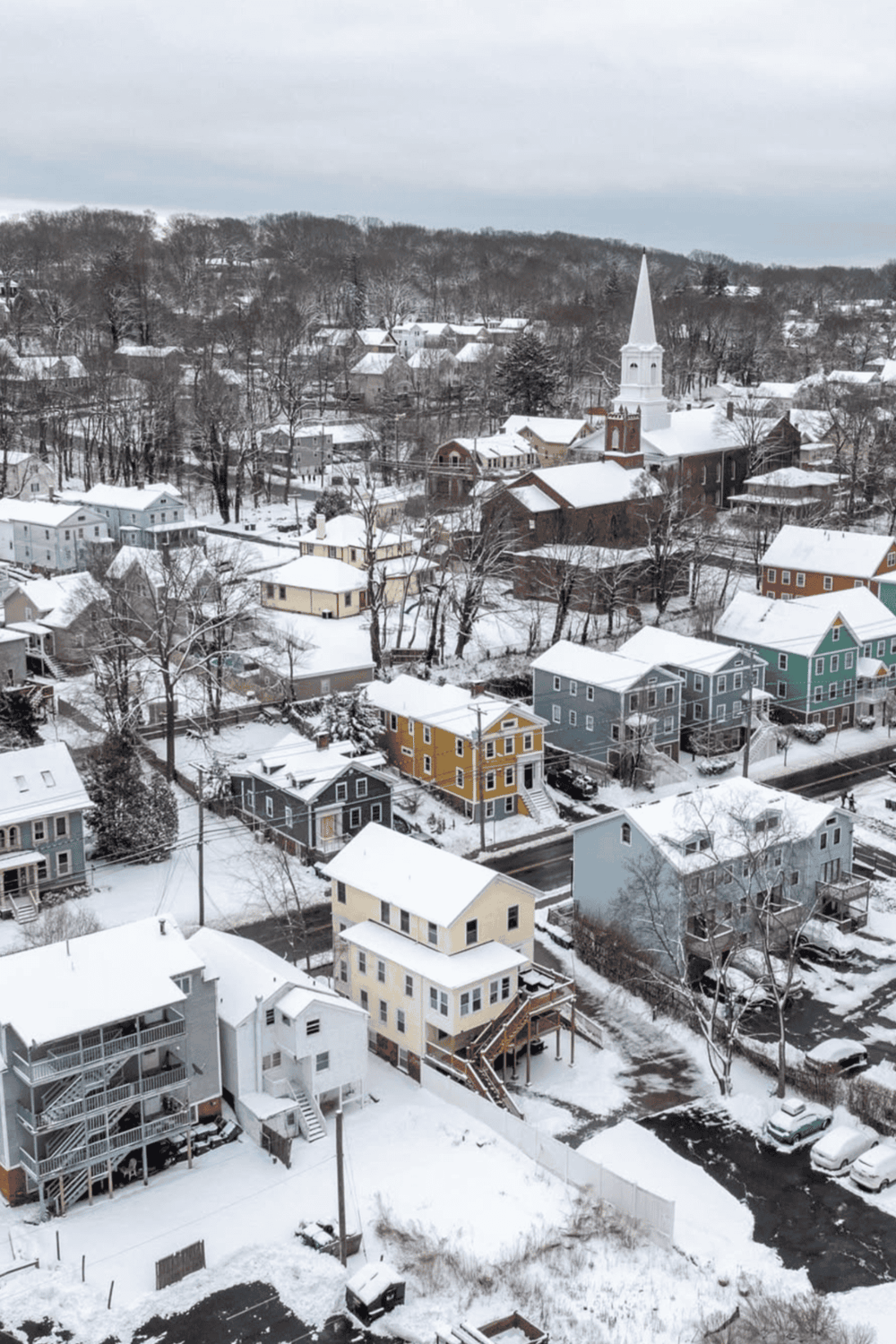 Colorful snow-covered houses in a quaint town with a prominent church steeple.