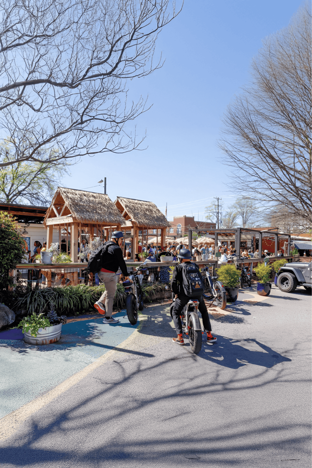 Biking in a lively outdoor community space with thatched-roof structures and social setting.