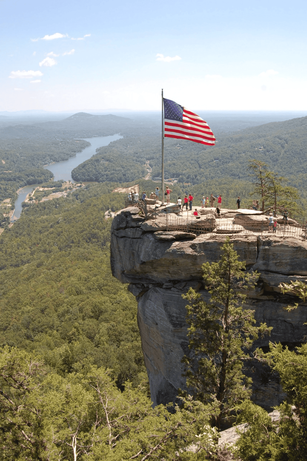 Breathtaking view of the American flag atop a cliff at Quest for Directions, overlooking lush forests and a winding river.