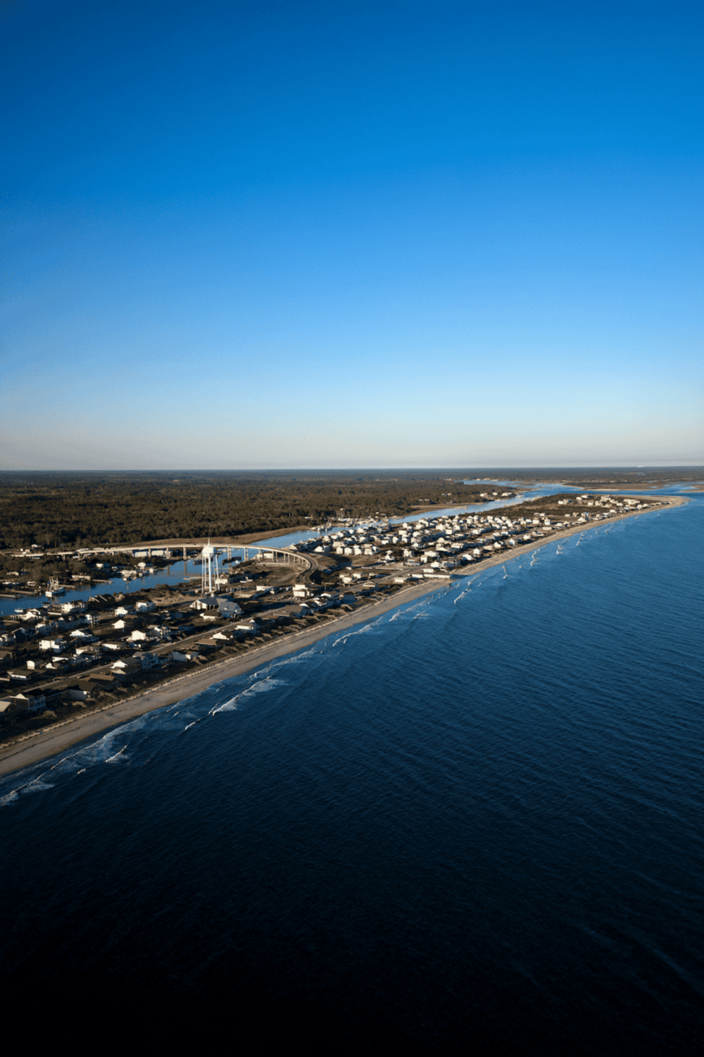 Seaside coastal town with ocean view and residential area, featuring a clear blue sky.