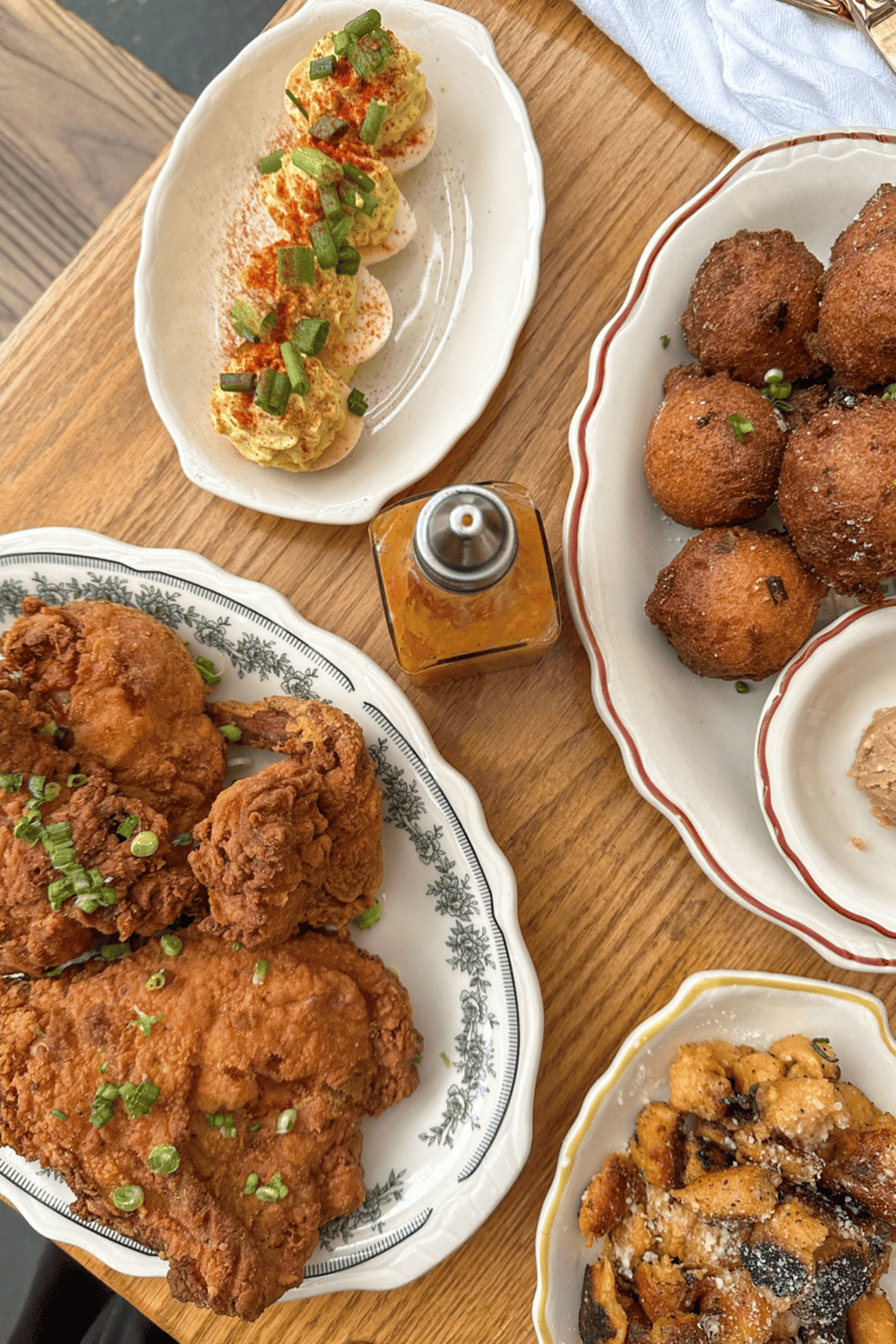 Crispy fried chicken, deviled eggs garnished with green onions, hushpuppies, and sweet potato fries on vintage dinnerware.
