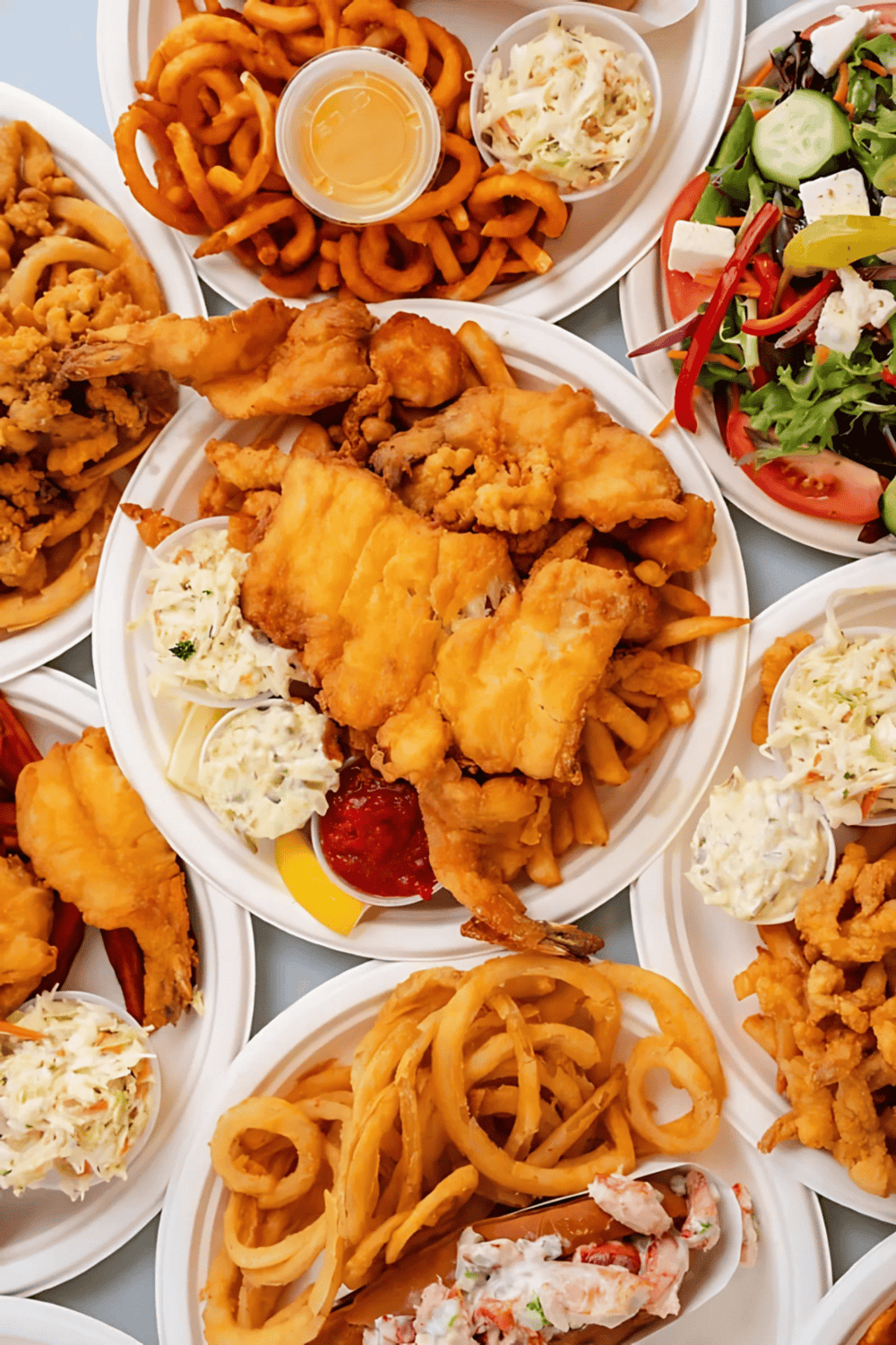 Fried chicken platter with coleslaw, onion rings, and salad on disposable plates.