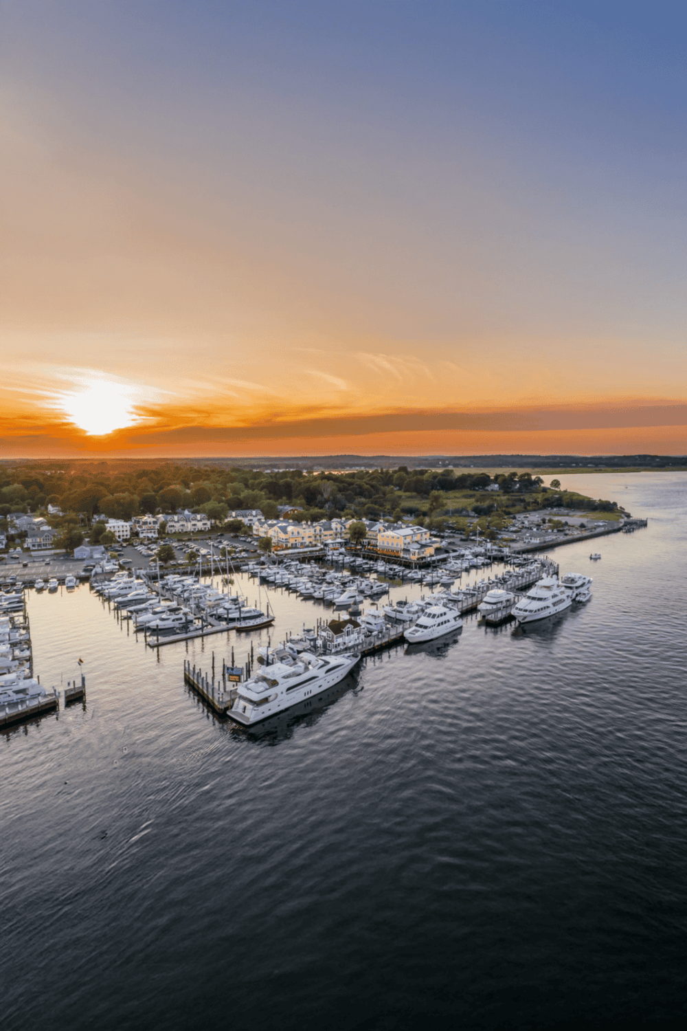 Boats and yachts docked at a marina during sunset, picturesque waterfront scene.