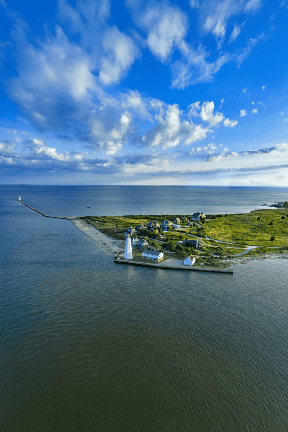 Aerial view of lighthouse and coastal village with ocean and cloudy sky, scenic travel destination.
